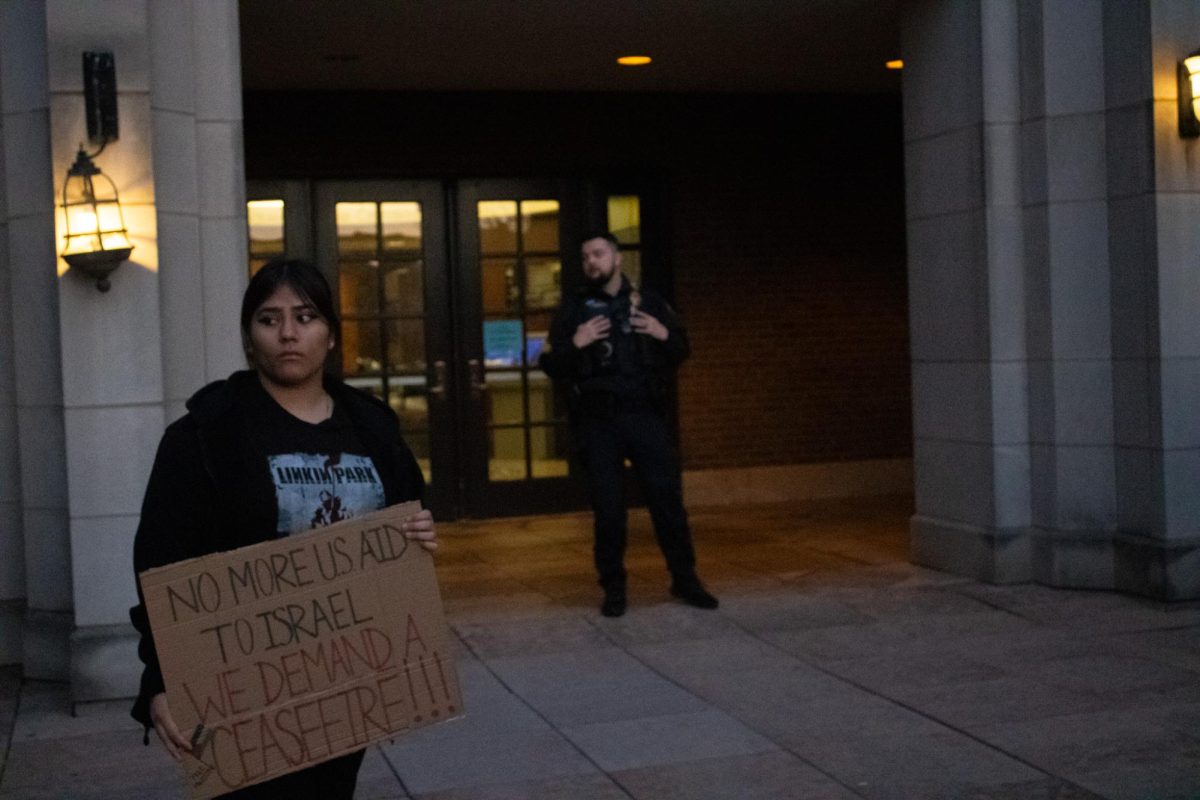 Student, Jazmine Carballido-Barrios, holds sign saying No more U.S. aid to Israel. We demand a ceasefire!!! in front of DPS officer blocking the doors.