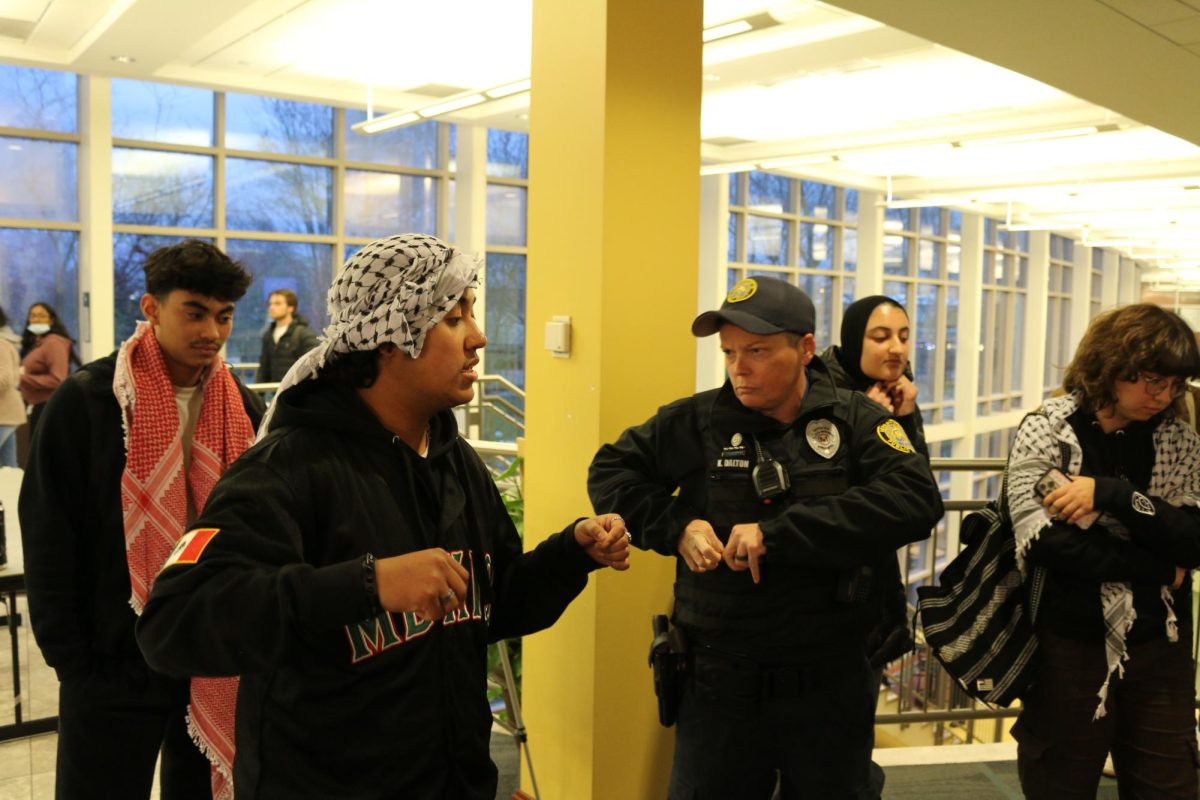 Sophomore Julian Garcia stands in BSC entryway as officer K. Dalton reaches for handcuffs in her vest, which she was reportedly holding the entire protest, at Saint Louis University on March 26.