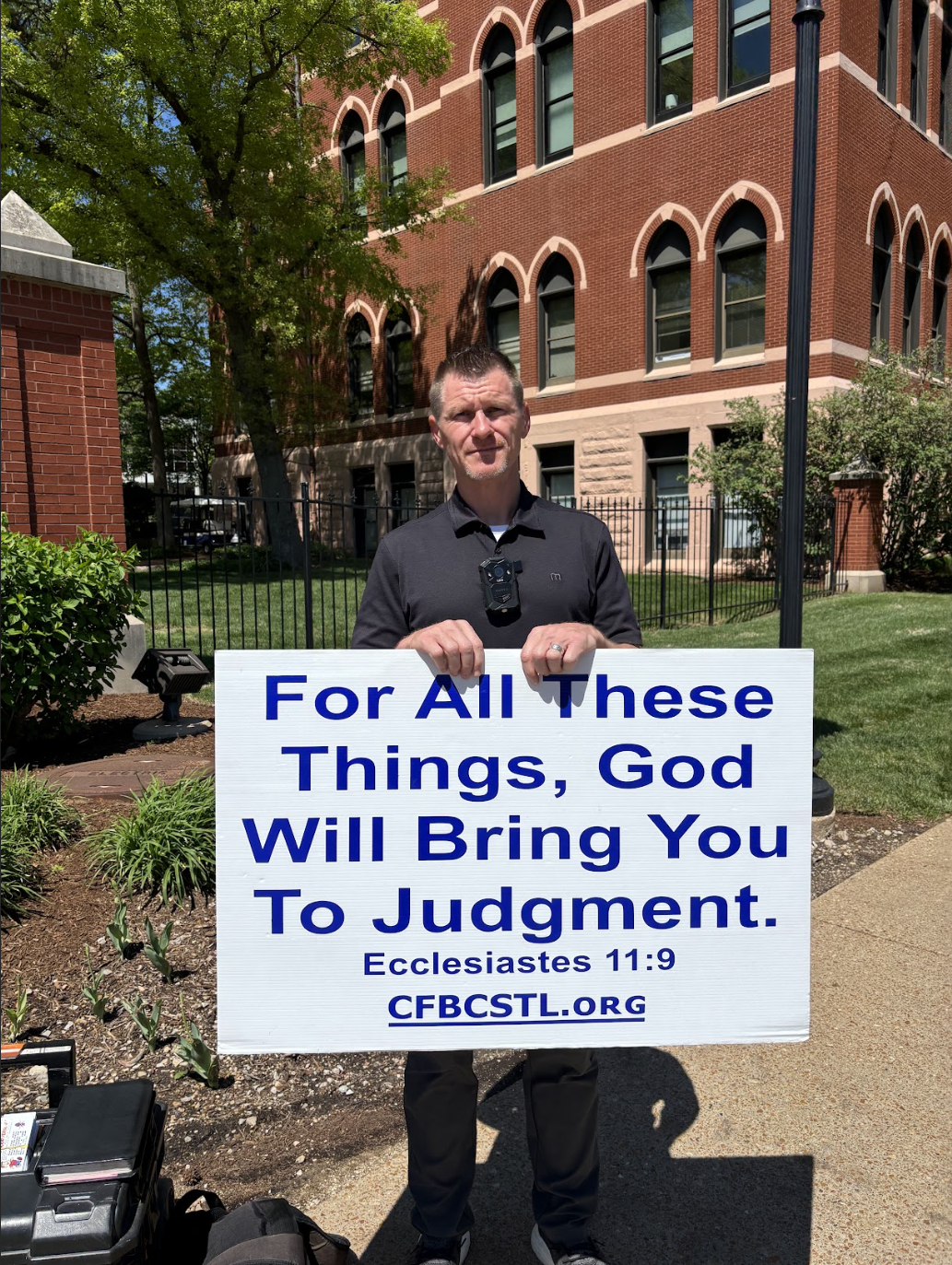 A street preacher, Geoffry R. Kirkland Elder-Shepherd, stands with a placard reading “For All These Things, God Will Bring You To Judgement Ecclesiastes 11:9” on the west side of the Grand Avenue crosswalk outside of Saint Louis University on April 16, 2026.